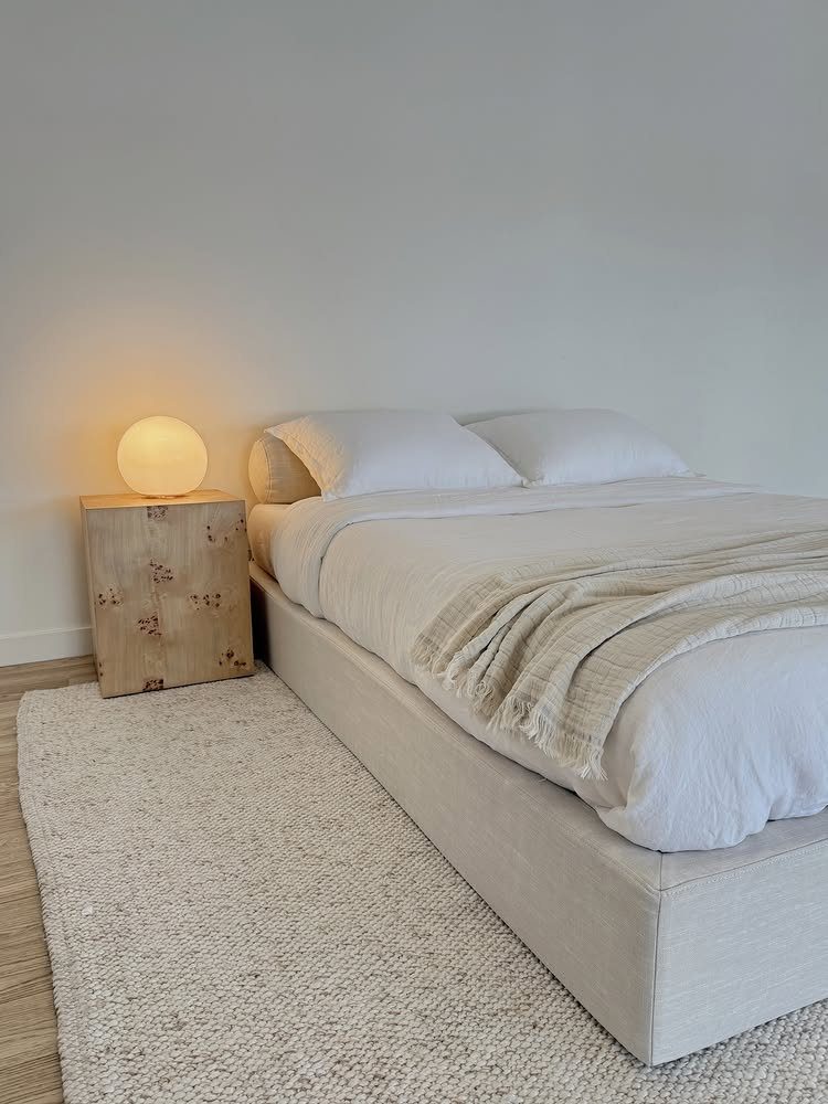 Minimalist bed with white linens and no headboard next to a wooden nightstand.