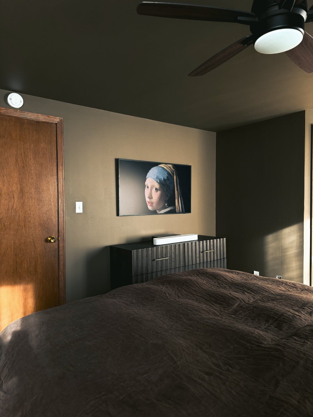 Dark brown bedroom featuring a bed, black dresser, and television showing a painting.