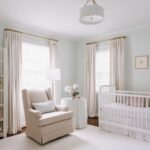 Pale blue-green nursery with a white crib, beige glider, and cream curtains.