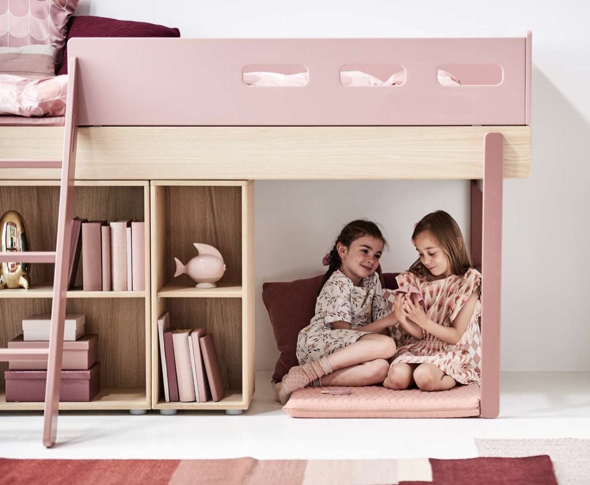 Two girls sitting under a pink and wood loft bed with safety rails.