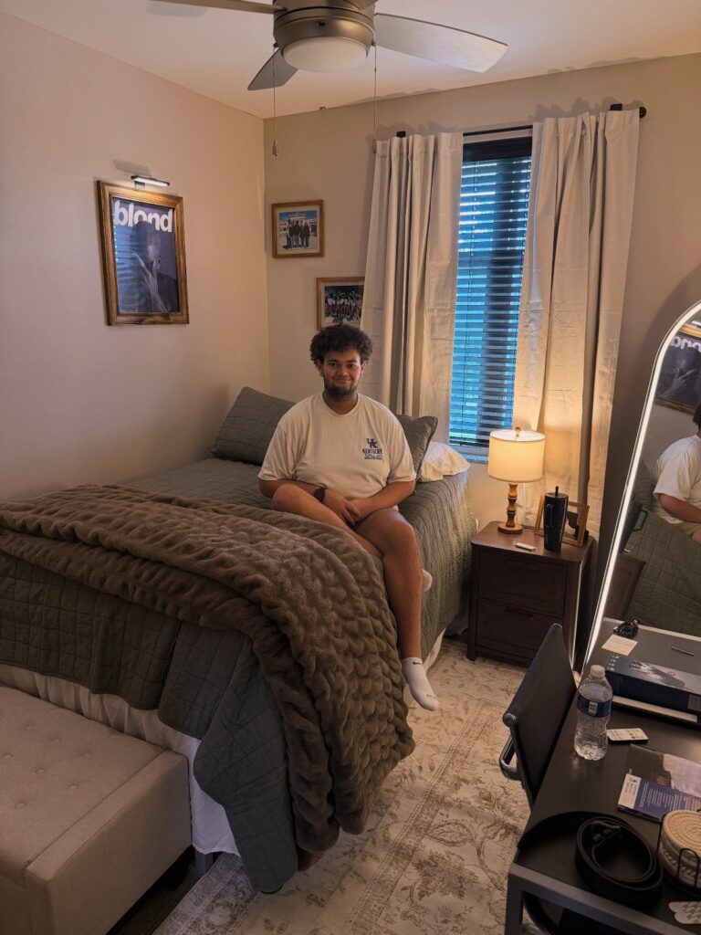 Young man sitting on a bed in a decorated dorm room with posters.