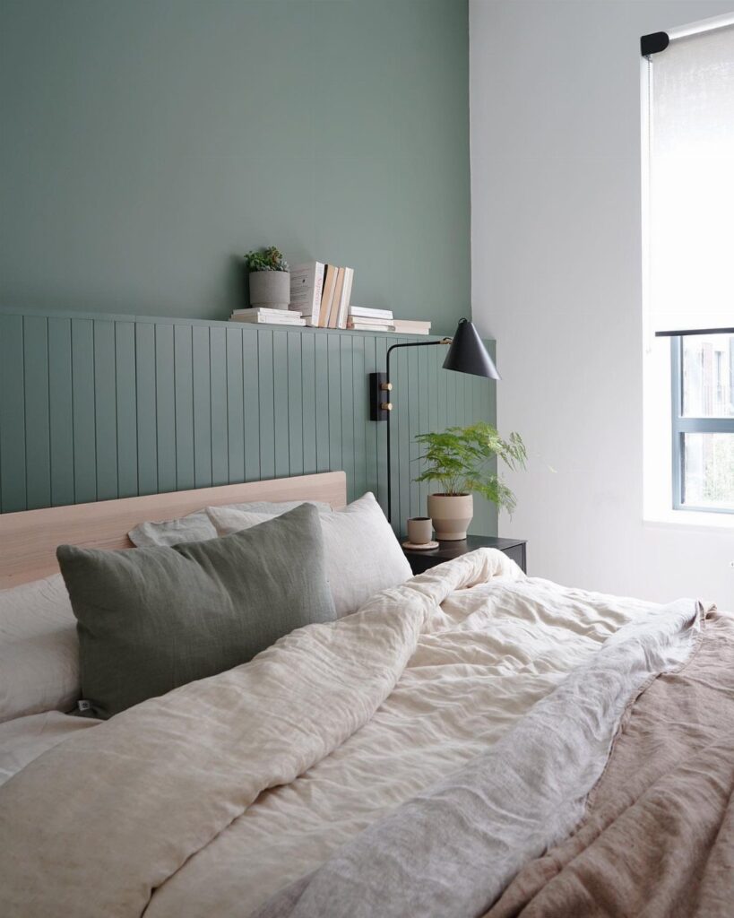 Light green bedroom walls with vertical paneling, white bedding, and a black lamp.