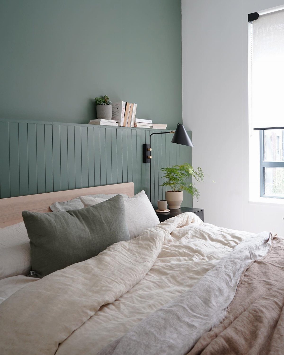 Light green bedroom walls with vertical paneling, white bedding, and a black lamp.
