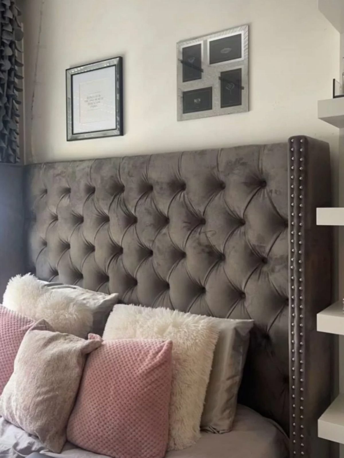 Grey velvet tufted headboard with nailhead trim and decorative pillows on a bed.