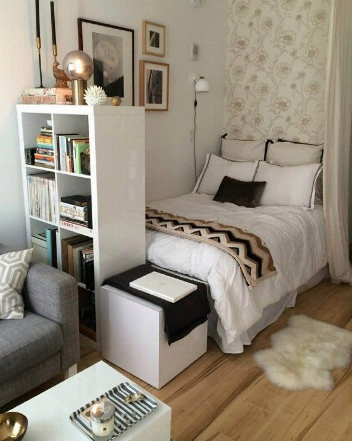 Studio apartment with a white bed separated from a grey sofa by a bookshelf.