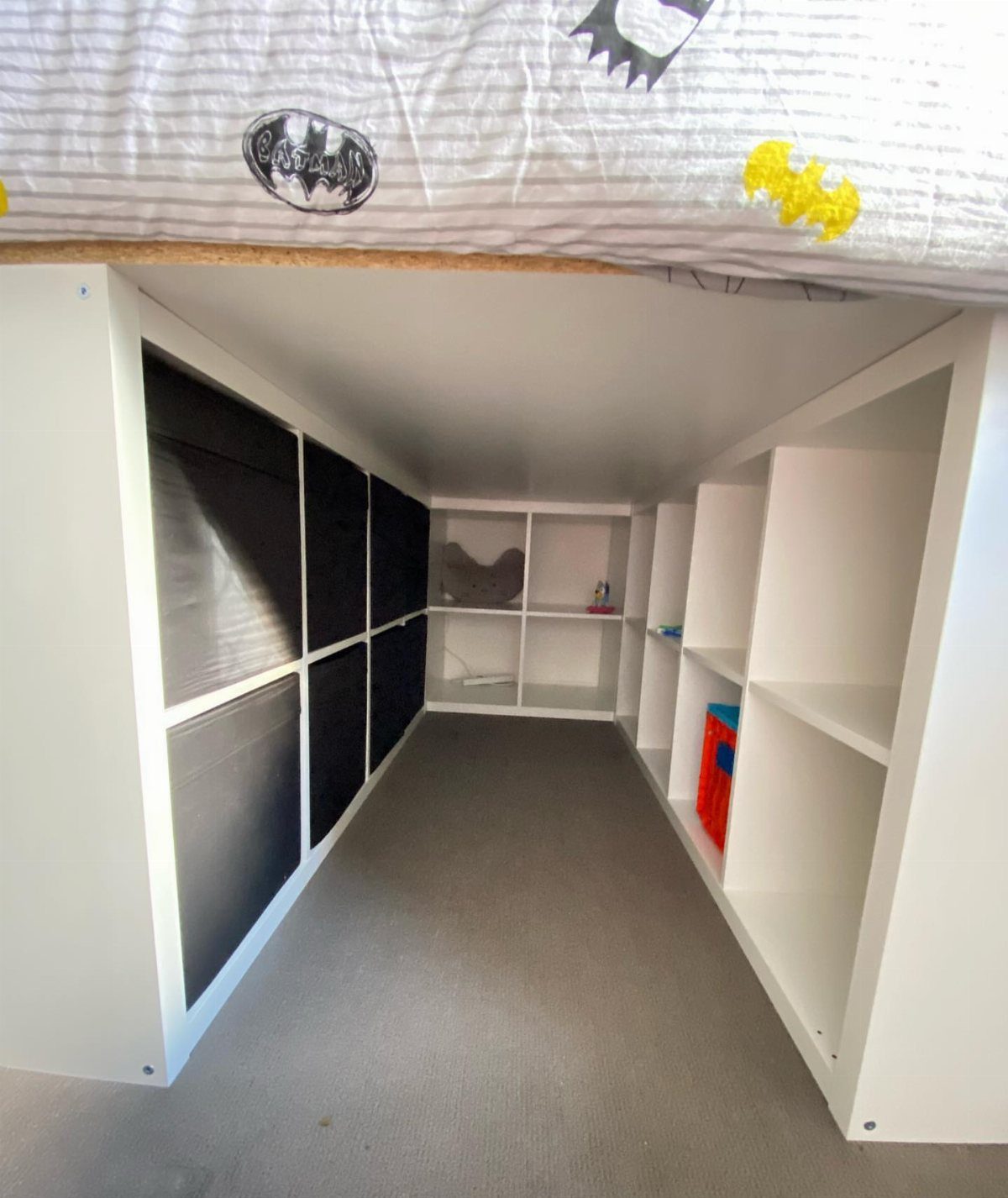 White loft bed with integrated shelving and black storage bins underneath.