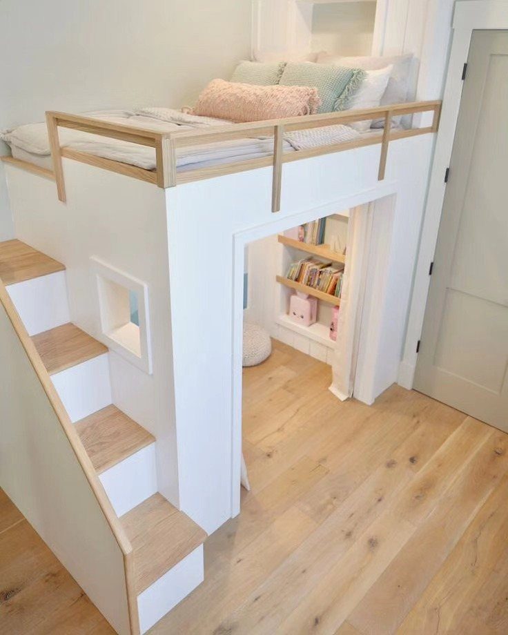 White junior loft bed with wooden stairs and a cozy reading nook underneath.