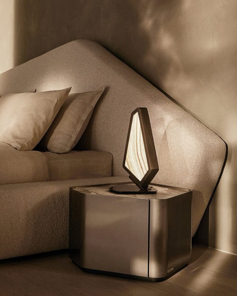 Geometric sculptural lamp on a metallic cubic table next to a curved beige sofa.