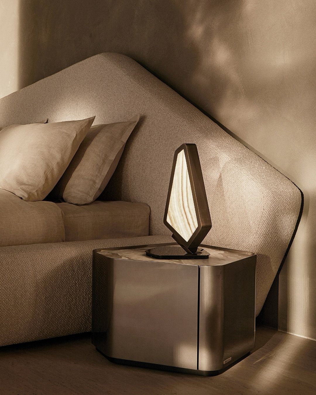 Geometric sculptural lamp on a metallic cubic table next to a curved beige sofa.