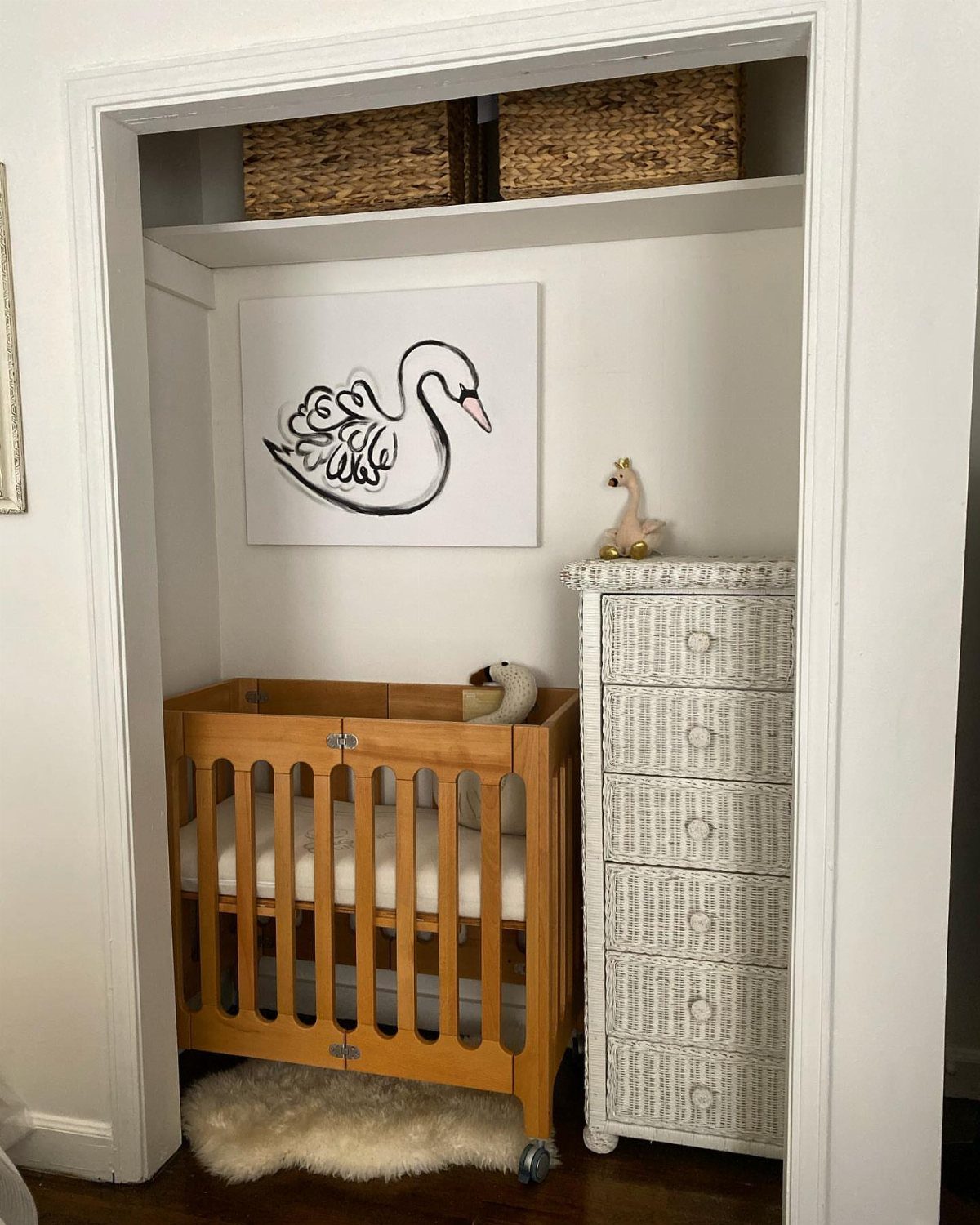 Wooden mini crib and white dresser in a small, white nursery nook.