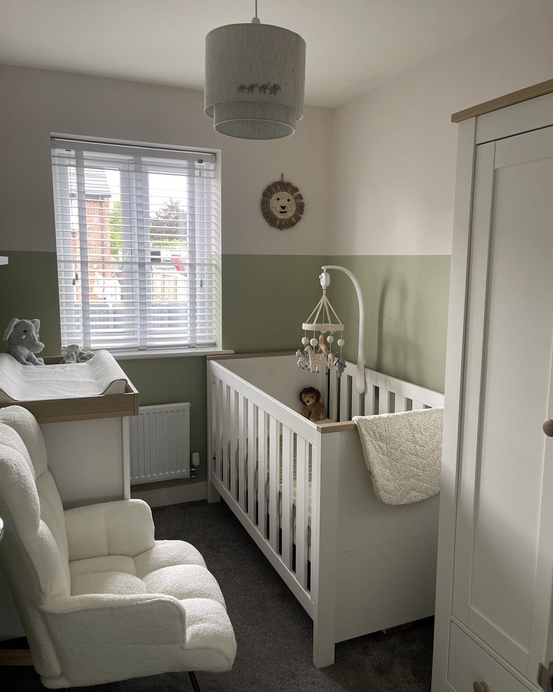 Small baby nursery with white crib, glider chair, and sage green walls.