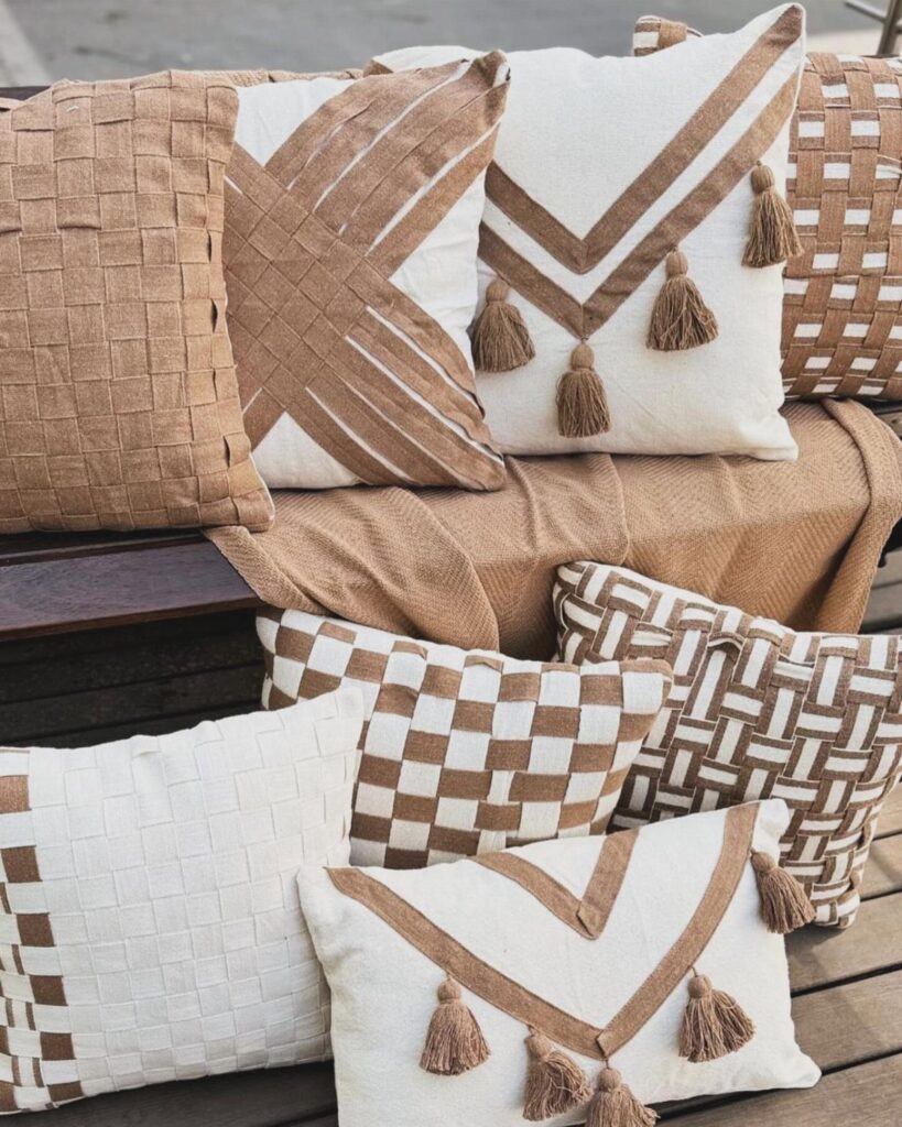 Assorted cream and tan throw pillows with woven textures and tassels on a deck.