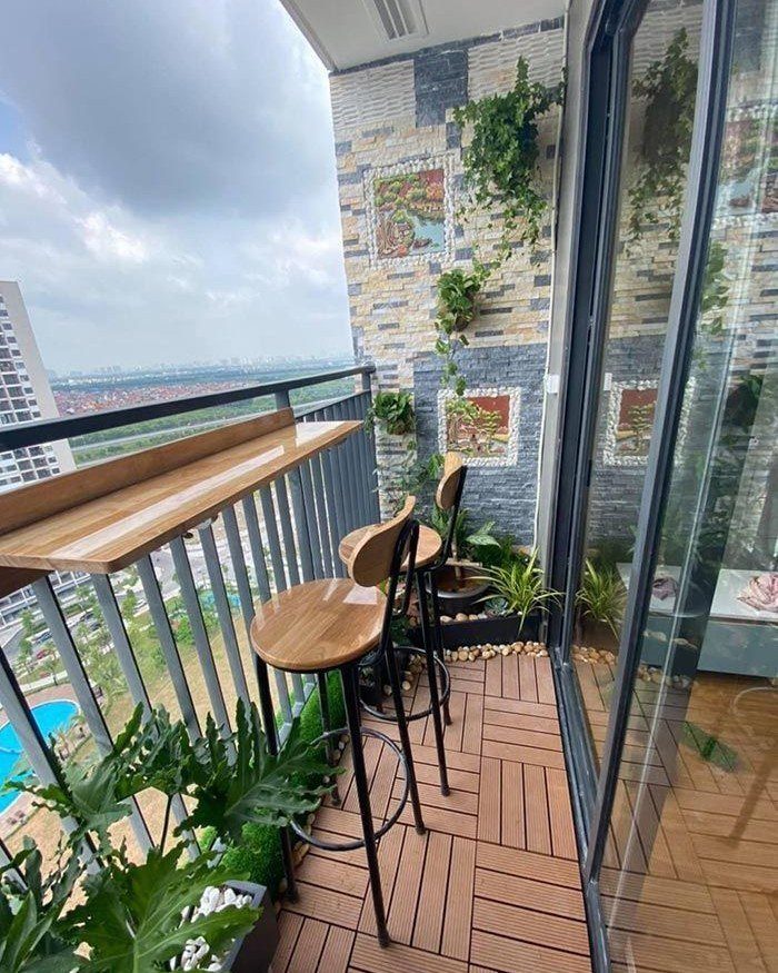 Balcony with wooden bar counter, stools, and greenery overlooking a city skyline.