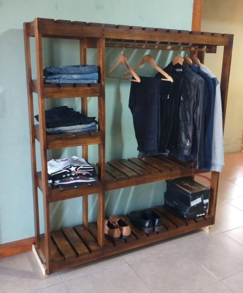 Wooden open clothing rack with shelves holding folded clothes, hanging jackets, and shoes.