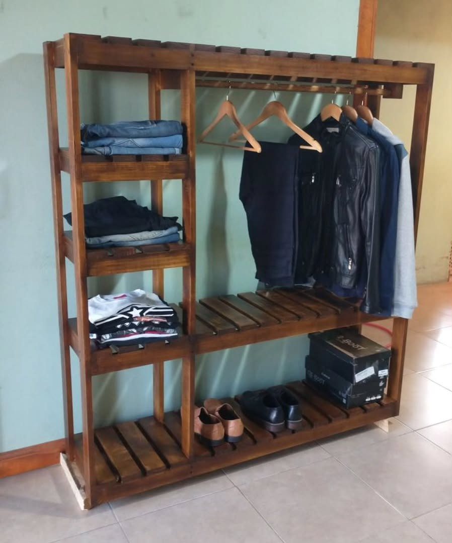 Wooden open clothing rack with shelves holding folded clothes, hanging jackets, and shoes.